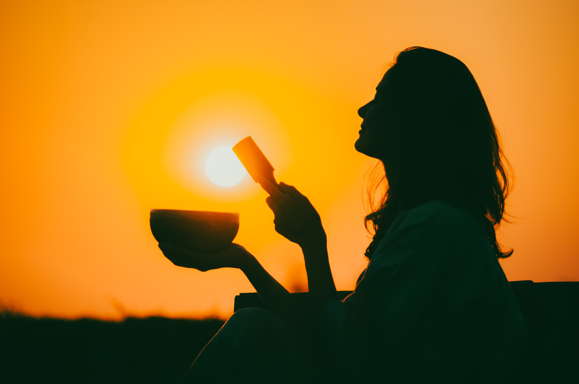 Silhouette of a Woman Playing a Tibetan Bowl at Sunset