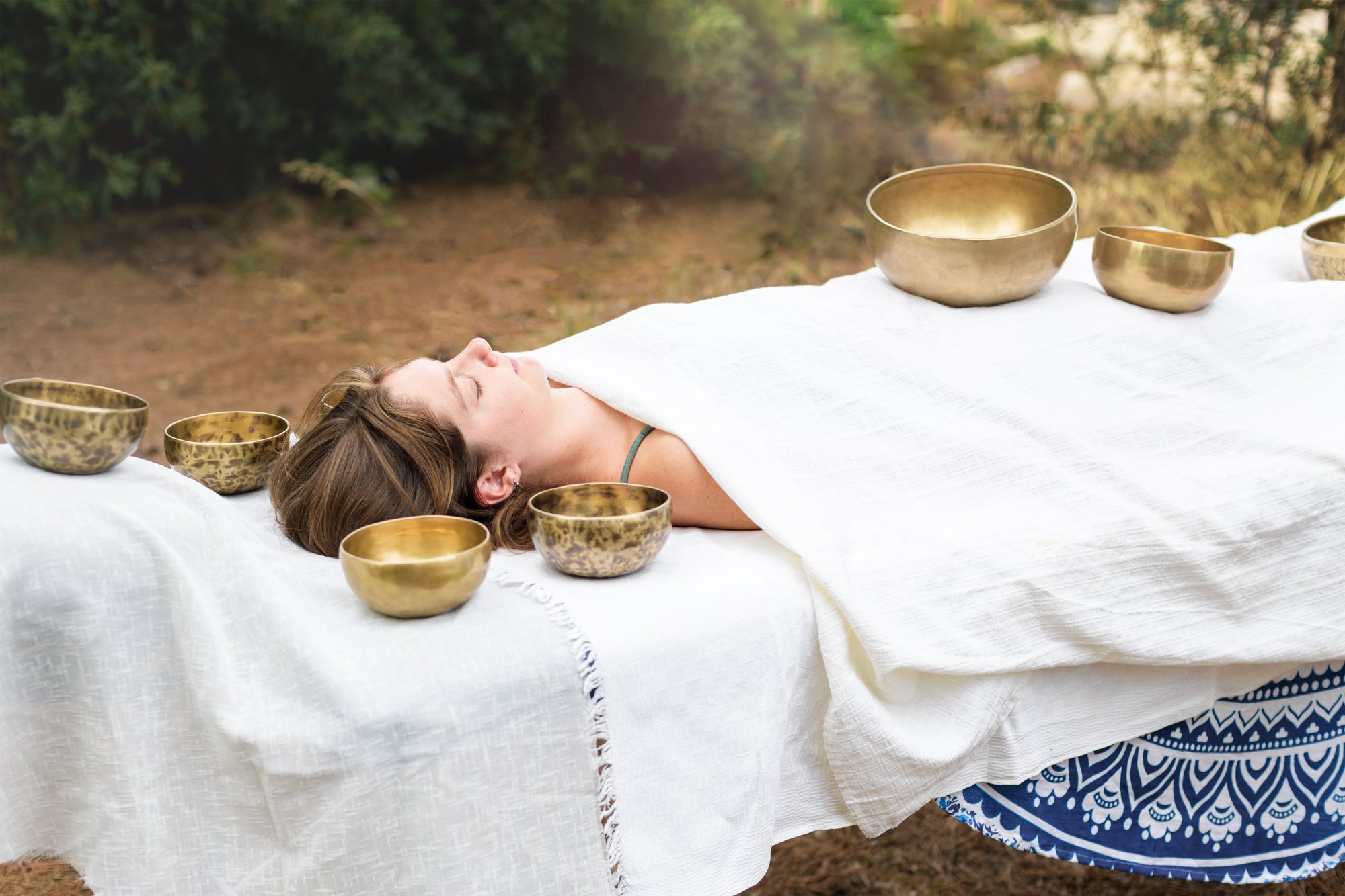 Young woman laying on a massage bed with tibetan singing bowl outdoor. Nepal copper singing bowl sound massage